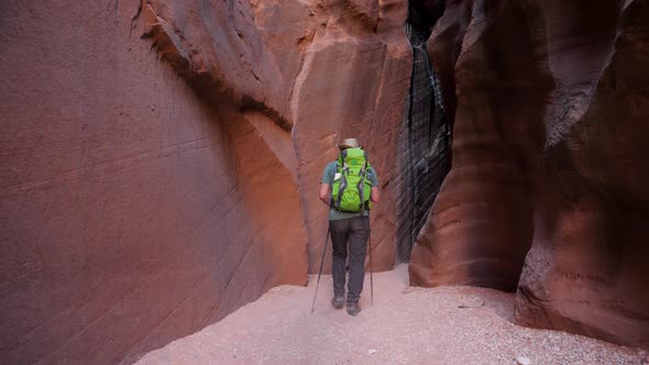 Hiker Hiking On Dry Riverbed In Cave Of Deep Slot Canyon With Orange Curve Rocks