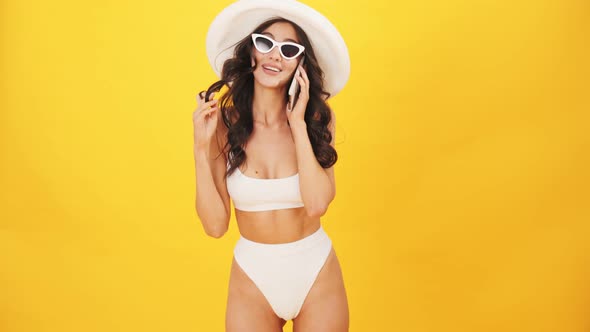 A cheerful brunette woman wearing a swimsuit talking on her mobile