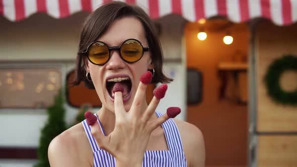 Stylish Caucasian Woman with Short Hair and Sunglasses Eats Raspberry From Fingers