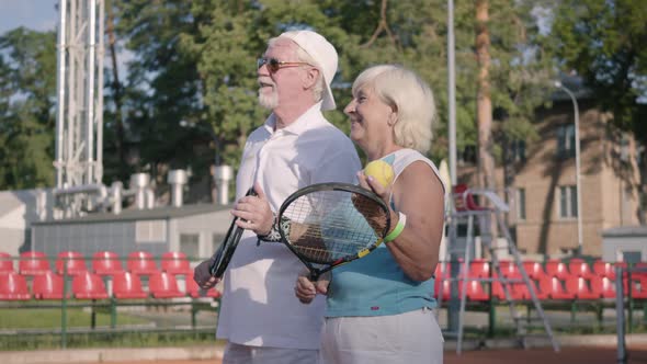 Cute Smiling Mature Couple for Getting Ready To Play Tennis on the Tennis Court