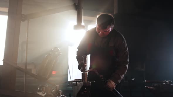 Man Blacksmith Shaping Hot Piece of Metal Using a Hammer