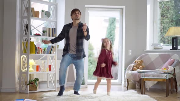 Funny Dance of Cheerful Young Father and Playful Cute Daughter Indoors at Home