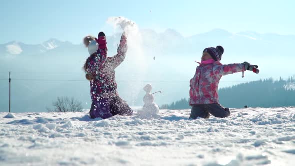 Cheerful Little Girls in Outwear Having Fun and Throwing Snow in Sunlight Standing Outdoors