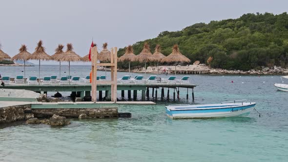 Empty Sun Loungers with Straw Umbrellas in Row on Pier By Beach in Turquoise Sea