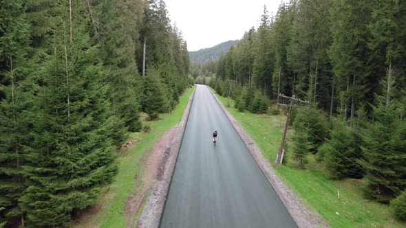 Cyclist in helmet on road bike fast riding on empty car road in pine tree forest