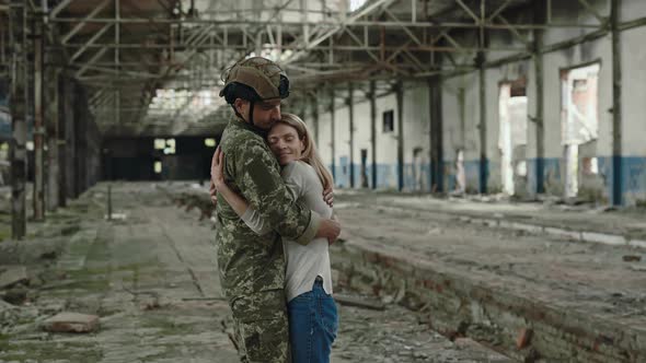 Loving Wife Hugging Strong Husband in Soldier Uniform While Standing Together at Destroyed Plant