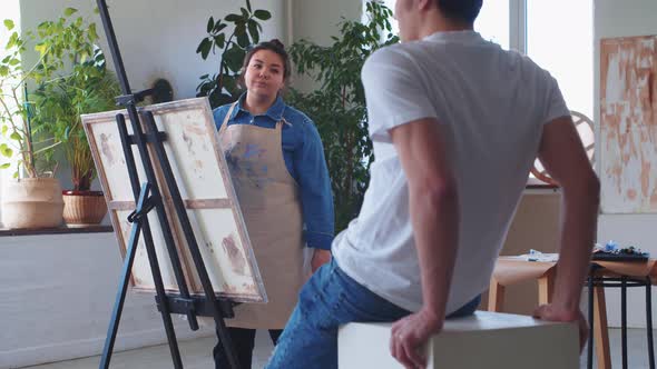 A Woman Paint Artist Drawing on a Canvas Taking a Male Model As a Reference