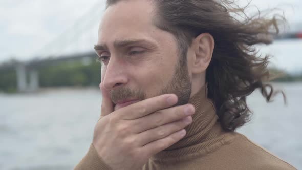 Close-up Face of Frustrated Young Man with Sore Eyes Standing Outdoors on Windy Day. Portrait of