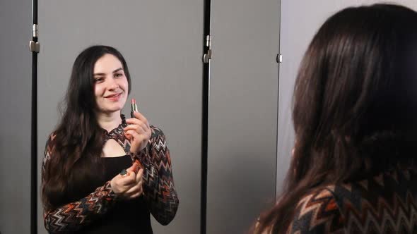 Beautiful Brunette Woman Dyes Her Lips with Lipstick in Front of the Mirror