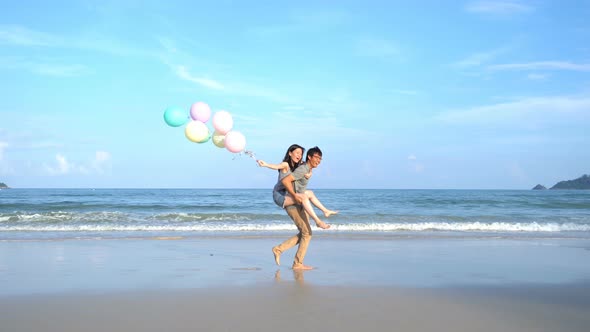 Happy Asian couple holding colorful balloons at the beach during travel trip on holidays