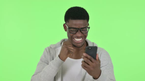 African Man Celebrating on Smartphone on Green Background