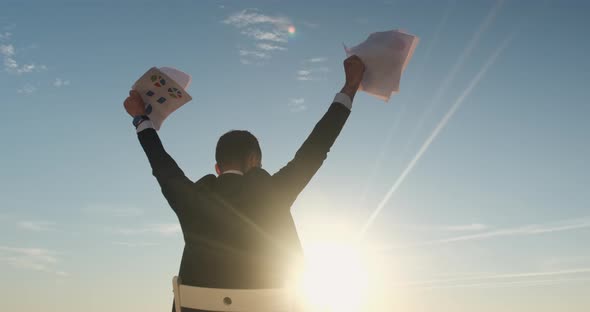 The businessman raises the sheets of paper up above his head.