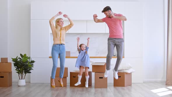 Happy new apartment owners family with little girl jump on brown wooden floor