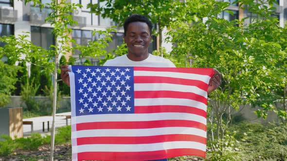 Portrait Smiling Afroamerican Man Holding an American Flag and Looks Camera