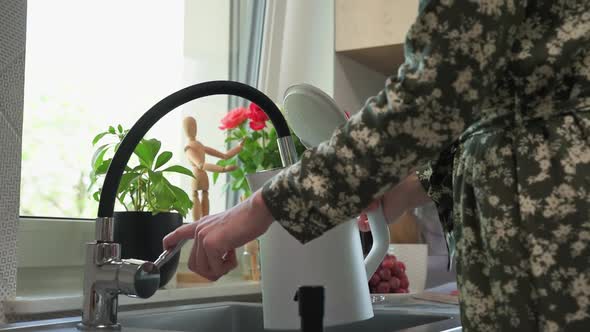 Woman Pouring Water From Faucet Into Electric Kettle at the Kitchen