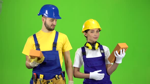 Pair of Builders Holding a Brick in Their Hands and Showing Their Fingers Up. Green Screen