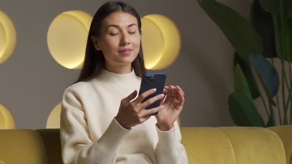 Cute Young Asian Woman Sitting on the Sofa in the Living Room of the House Making Online Purchases