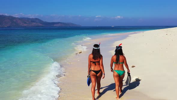 Pretty fun women on photoshoot in the sun at the beach on paradise white sand and blue 4K background