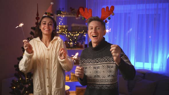 Happy Smiling Couple Woman in Festive Elf Cap and Man in Red Deer Horns Headband Dances with