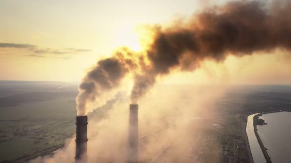 Aerial view of coal power plant high pipes with black smoke moving up polluting atmosphere at sunset