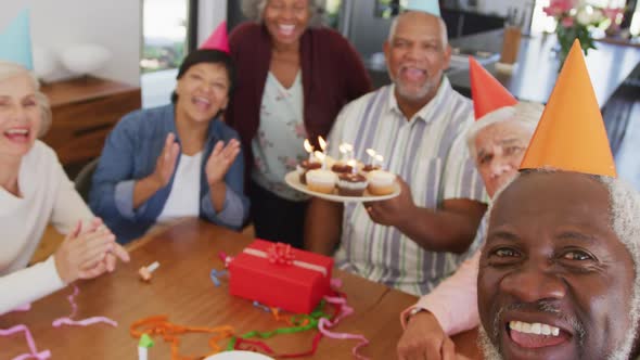 Portrait of happy senior diverse people at birthday party with cake and gifts at retirement home