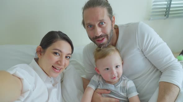 Caucasian Parents couple using mobile phone with little baby boy video call online with family.