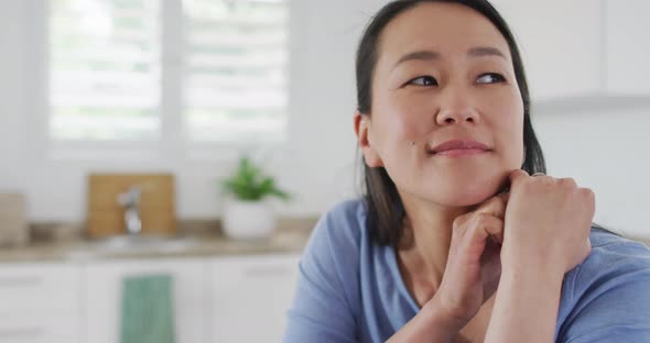 Portrait of happy asian woman sitting in kitchen