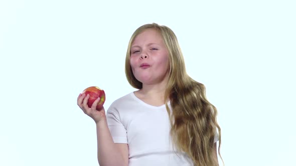 Little Girl Bites an Apple and Shows a Thumbs Up. White Background. Slow Motion