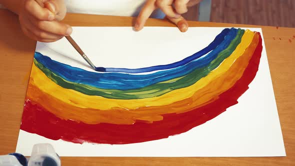 A Child's Hand Draws a Large Rainbow with Colored Paints on a Sheet