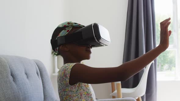 African american girl gesturing while using vr headset sitting on the couch at home