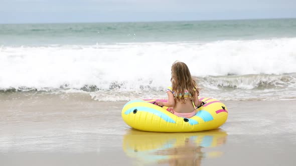 Young girl sitting on float tube at the beach waiting for a wave to roll in