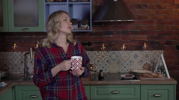 Happy Woman in the Kitchen at Home Drinks Coffee From a Mug