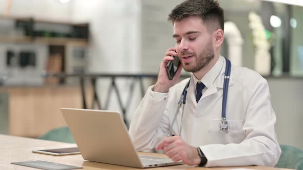 Young Doctor with Laptop Talking on Smartphone in Office 