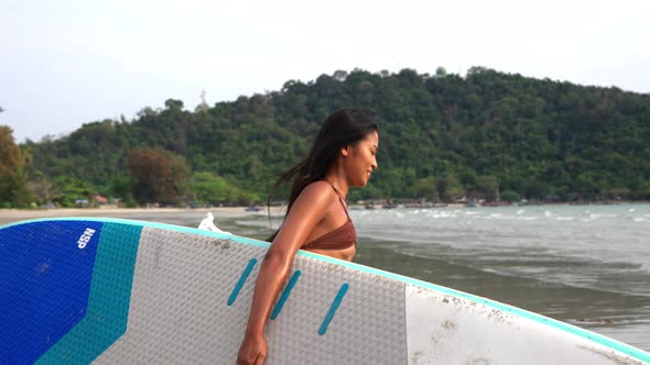 Young Woman Carrying Paddle Board On Beach