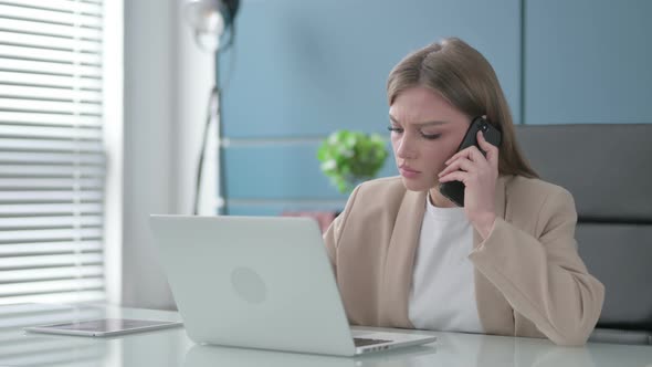 Businesswoman Talking on Smartphone While Using Laptop in Office