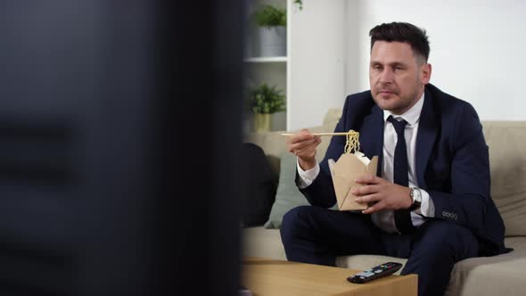 Businessman Watching TV, Eating Wok Noodles and Drinking Coffee at Home