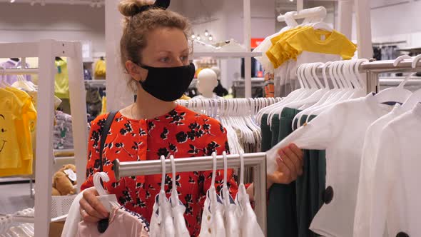 A Girl with Hair Bun Wearing Face Mask Picking an Outfit in Clothing Store. Safe Shopping During