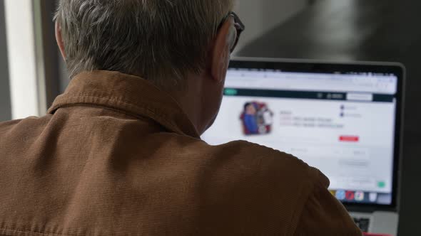 Old man in eyeglasses using laptop computer at home.