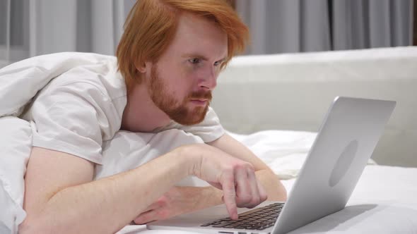 Thinking Redhead Beard Man Working on Laptop Lying in Bed