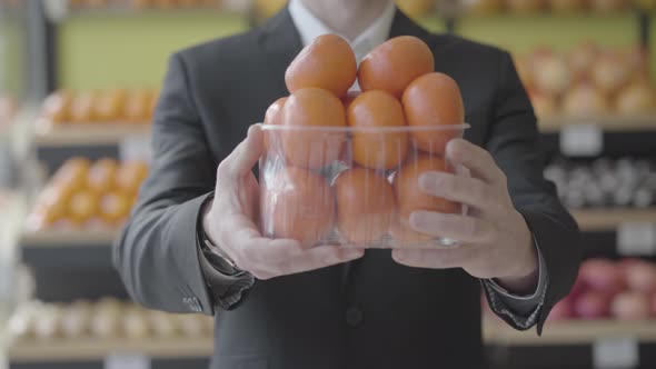 Unrecognizable Caucasian Man in Suit Stretching Basket of Delicious Juicy Tangerines To Camera. Male