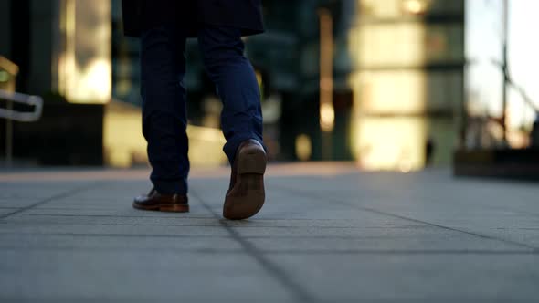 Men's Feet in Blue Plaid Trousers and Brown Shoes Walk Along the Pavement Slabs Against the