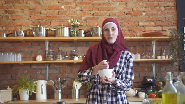 Pretty Muslim Young Woman in a Scarf Prepares in the Kitchen