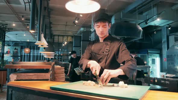 A Cook in Uniform is Chopping Mushrooms on the Counter