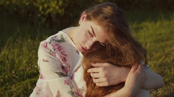 Portrait of Young Girl Sitting in Pose with Hugged Knees Among Field Grass