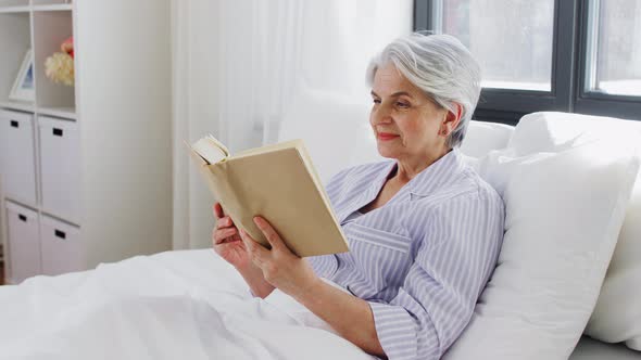 Senior Woman Reading Book in Bed at Home Bedroom