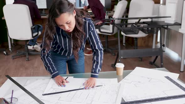 Young Female Architect Drawing Line on Blueprints