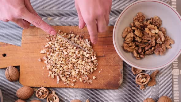 Chopping Walnuts Cores with Kitchen Knife on a Wood Cutting Board