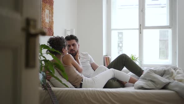 Young American Couple is Talking and Hugging While Lying on Bed in White Bedroom Spbd