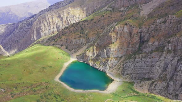 Flying Around a Mountain Lake with Turquoise Water and Green Grass. Reflection Sky and Clouds in the