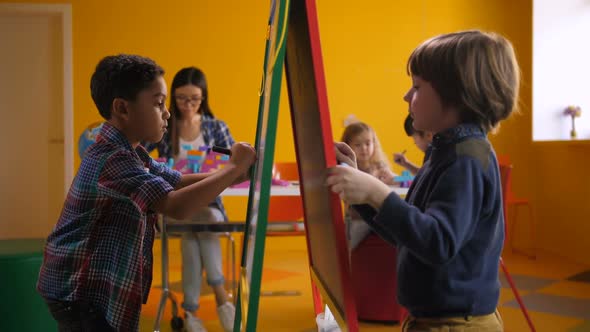 Diverse Boys Drawing and Painting on Easel Board